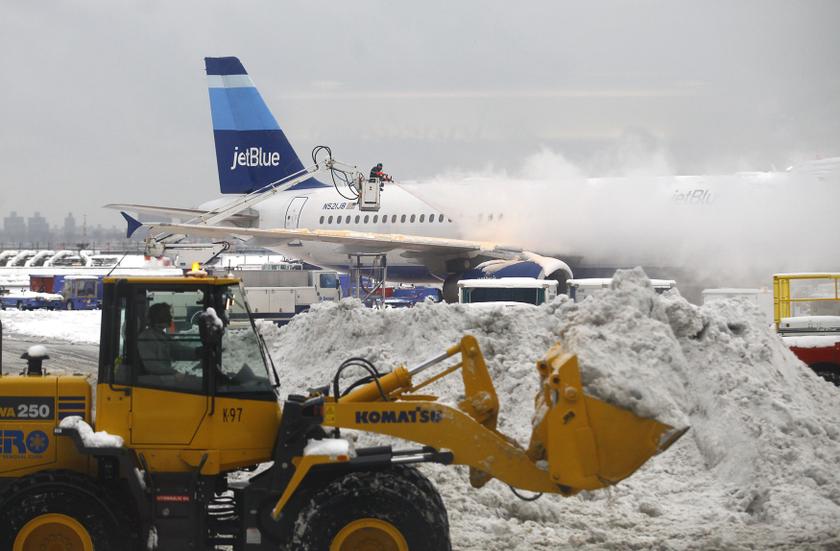 A worker de-ices an airplane sitting at a gate near terminal C as a man in a tractor removes snow from the tarmac at LaGuardia Airport in the Queens borough of New York in this file photo. u00e2u20acu201d Reuters pic