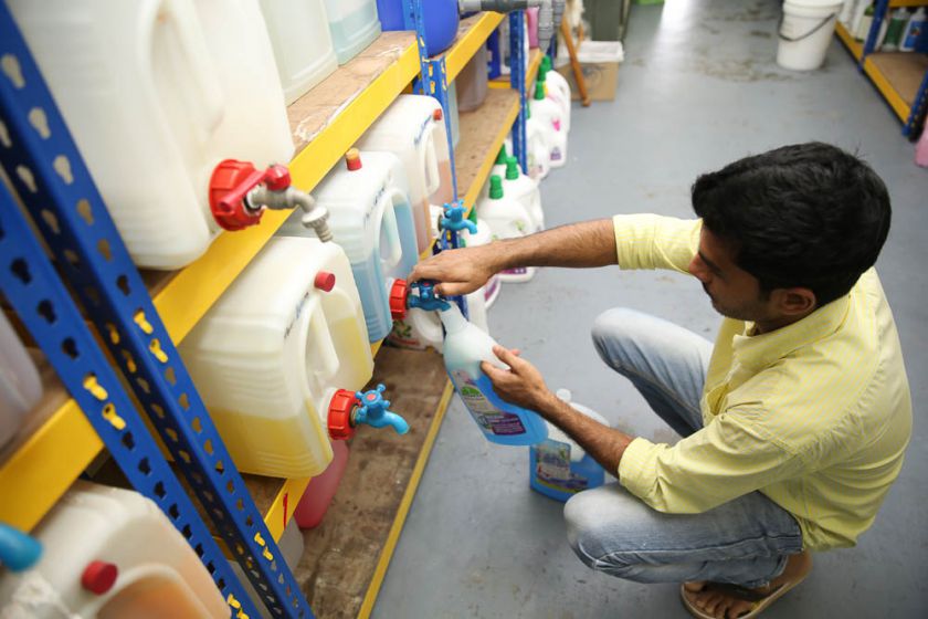 A worker refills floor cleaning liquid into used bottles for a customer.
