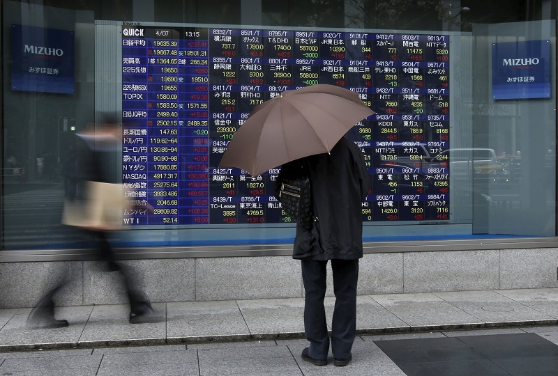 A man holding an umbrella looks at an electronic stock quotation board outside a brokerage in Tokyo, April 7, 2015. u00e2u20acu201d Reuters pic