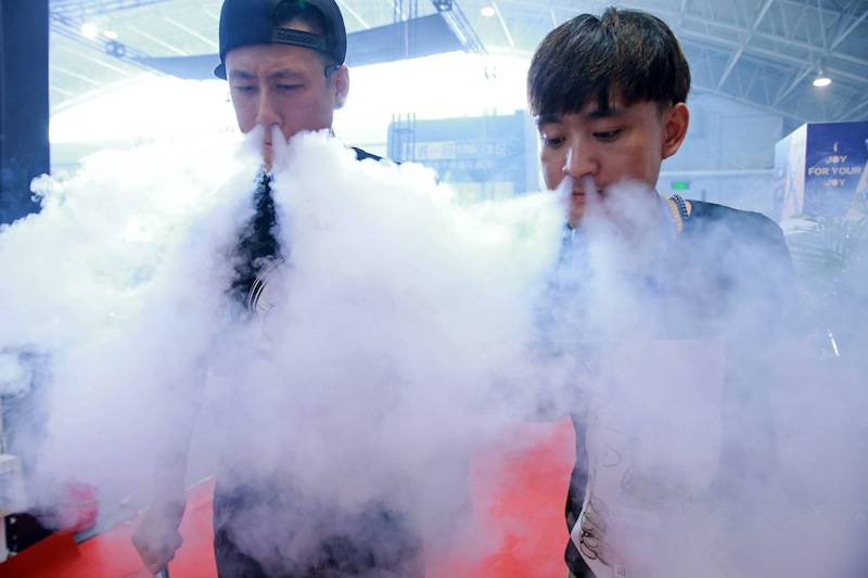 This picture taken on July 23, 2015 shows sales staff exhaling vapour while demonstrating their electronic cigarette products at the Beijing International Vapor Distribution Alliance Expo in Beijing. u00e2u20acu201d AFP pic