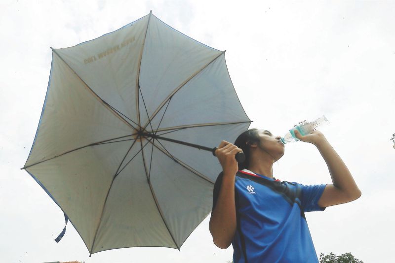 Shazli Zahari, 23, quenches his thirst by drinking water as he uses an umbrella to protect himself from the sun. u00e2u20acu201d Picture by Farhan Najib