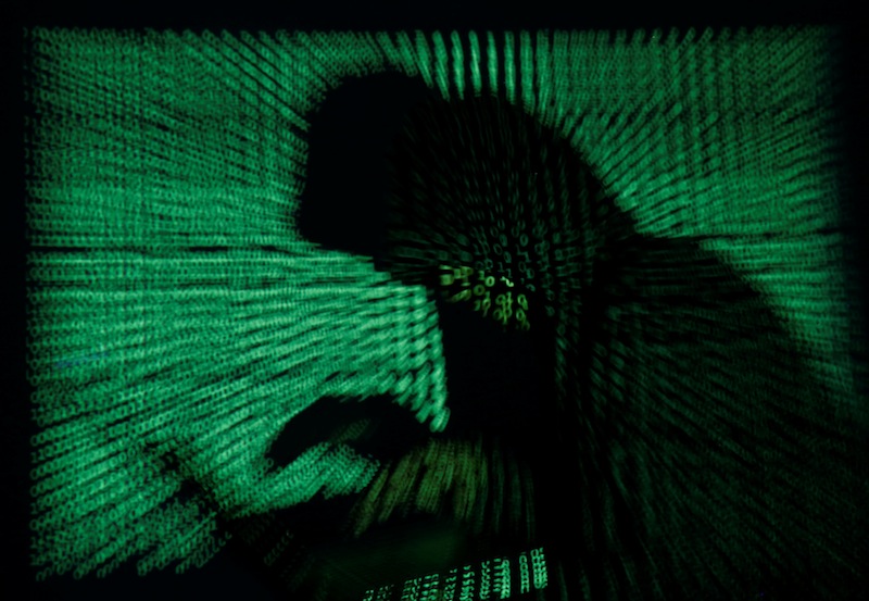 A hooded man holds a laptop computer as cyber code is projected on him in this illustration picture taken on May 13, 2017. u00e2u20acu201d Reuters pic