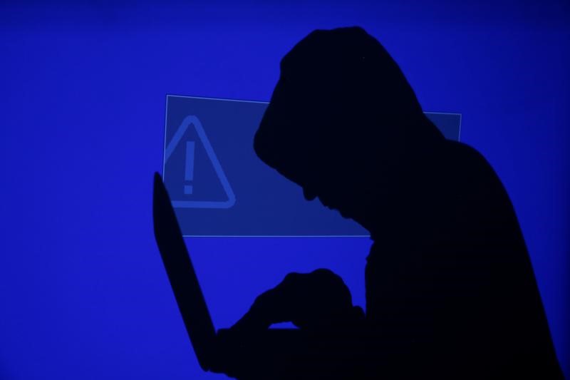 A hooded man holds a laptop computer as blue screen with an exclamation mark is projected on him in this illustration picture taken on May 13, 2017. u00e2u20acu201d Reuters pic