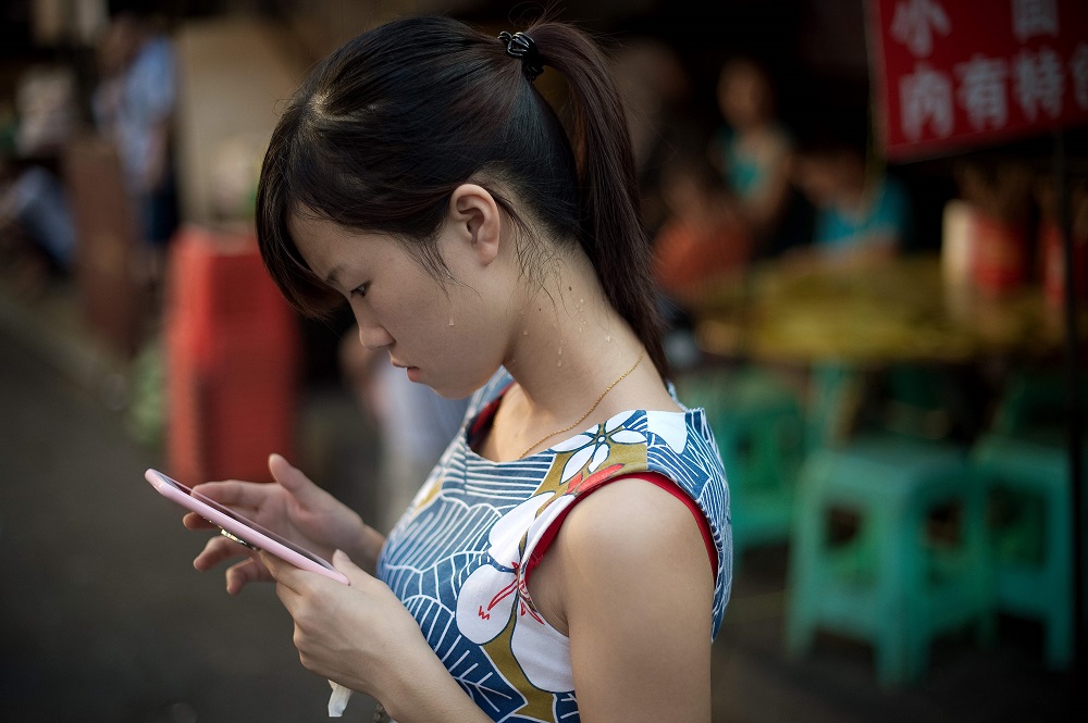 This file picture taken on August 24, 2016 shows a young woman looking at her smartphone in Chongqing. u00e2u20acu201d AFP pic 