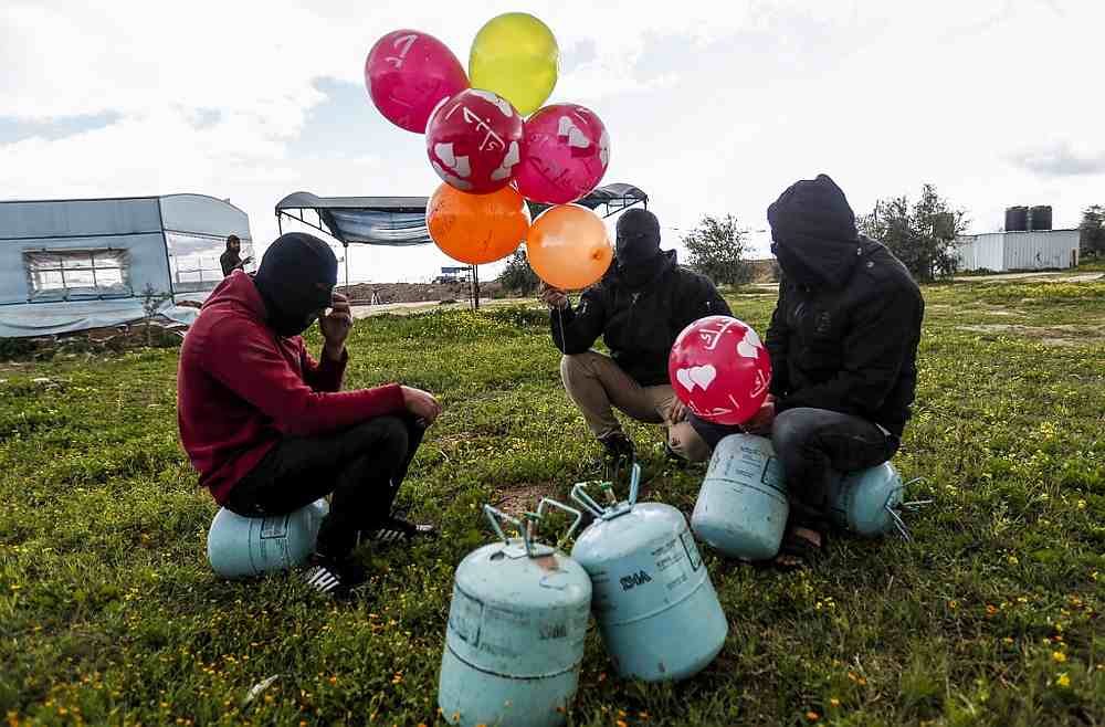 Masked Palestinians prepare to attach balloons to a gas canister before releasing it near Gaza's Bureij refugee camp, along the Israel-Gaza border fence February 10, 2020. — AFP Masked Palestinians prepare to attach balloons to a gas canister before releasing it near Gaza's Bureij refugee camp, along the Israel-Gaza border fence February 10, 2020. — AFP