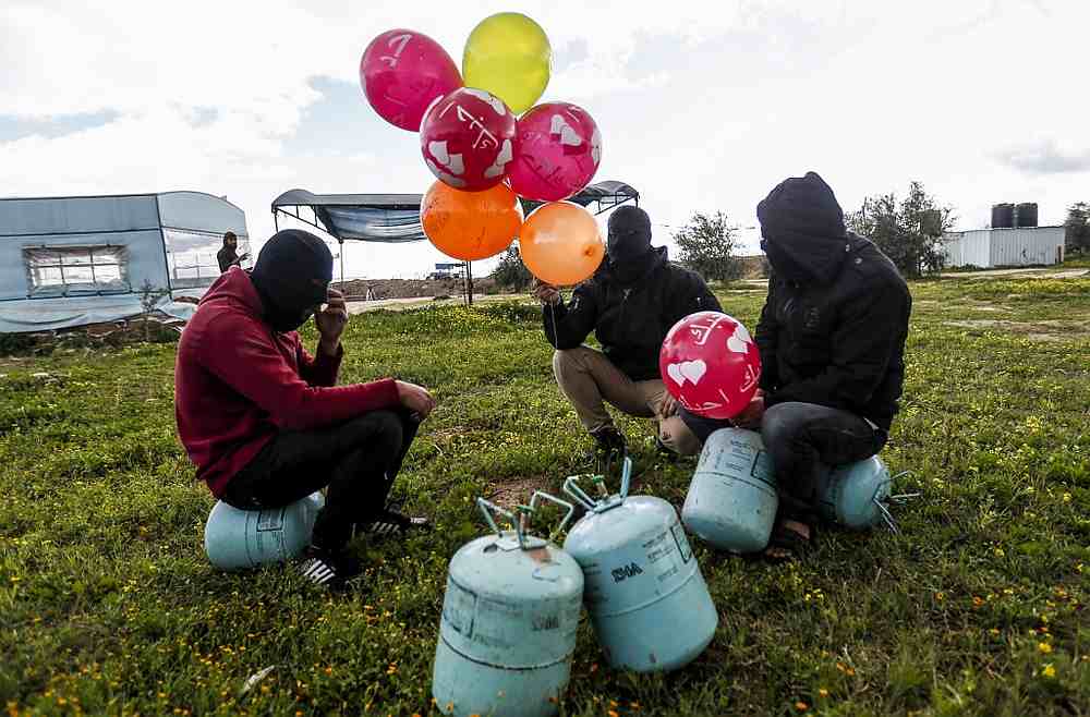 Masked Palestinians prepare to attach balloons to a gas canister before releasing it near Gaza's Bureij refugee camp, along the Israel-Gaza border fence February 10, 2020. u00e2u20acu201d AFP