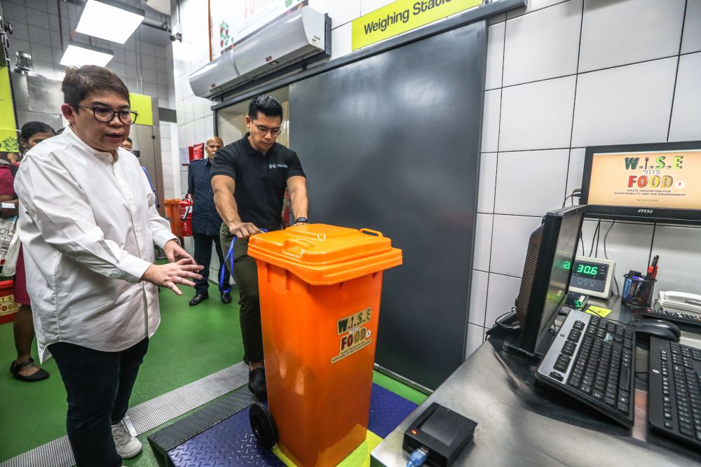 Lee and co-founder of Microbs, John Hans Oei, demonstrating that all restaurant tenants need to weigh their bins first before the other processes at the management system can take place. — Picture by Firdaus Latif