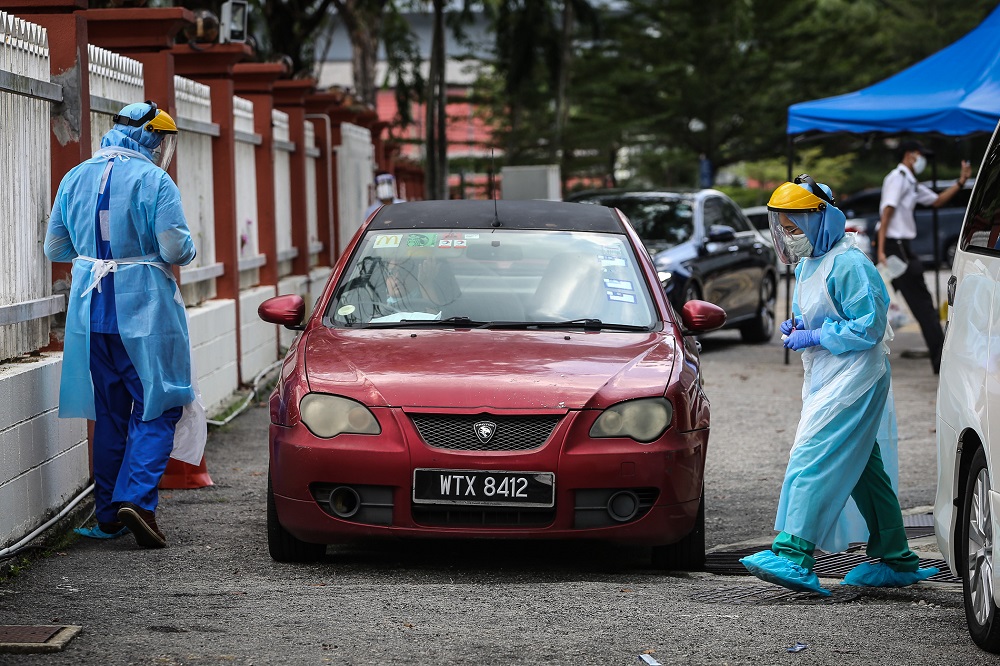 A health worker in protective suit swabs a driveru00e2u20acu2122s mouth at a drive-through testing site for Covid-19 at KPJ Damansara Specialist Hospital in Petaling Jaya March 28, 2020. u00e2u20acu201d Picture by Yusof Mat Isa