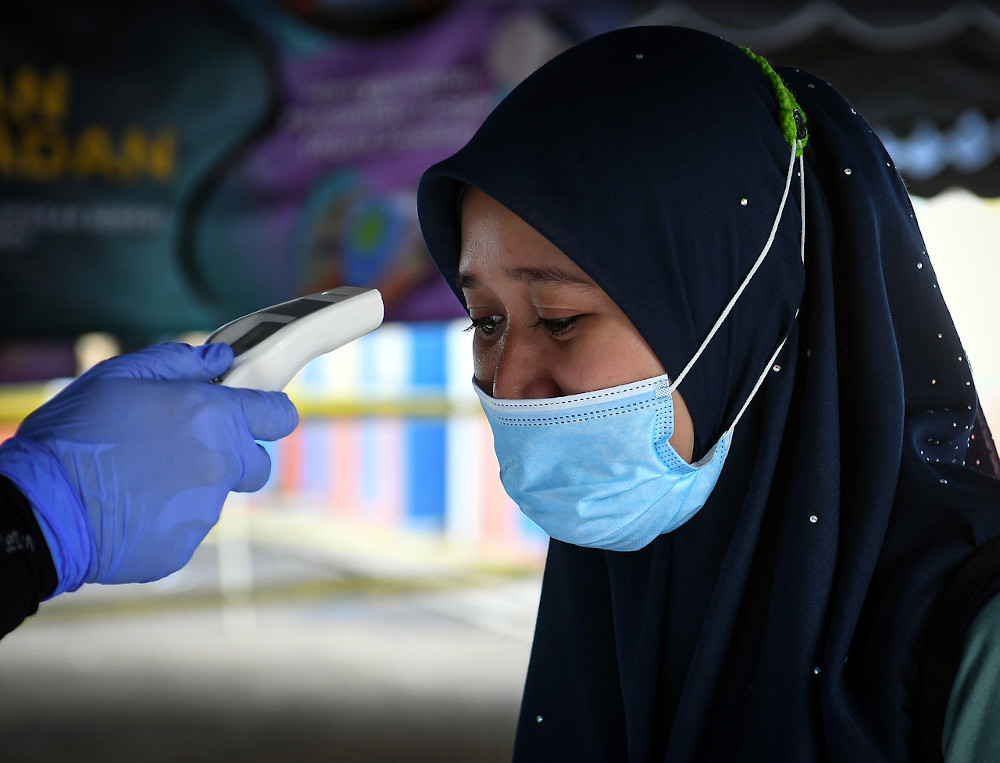 An official takes the temperature of a voter outside the voting centre for the Chini by-election July 4, 2020. u00e2u20acu201d Bernama pic