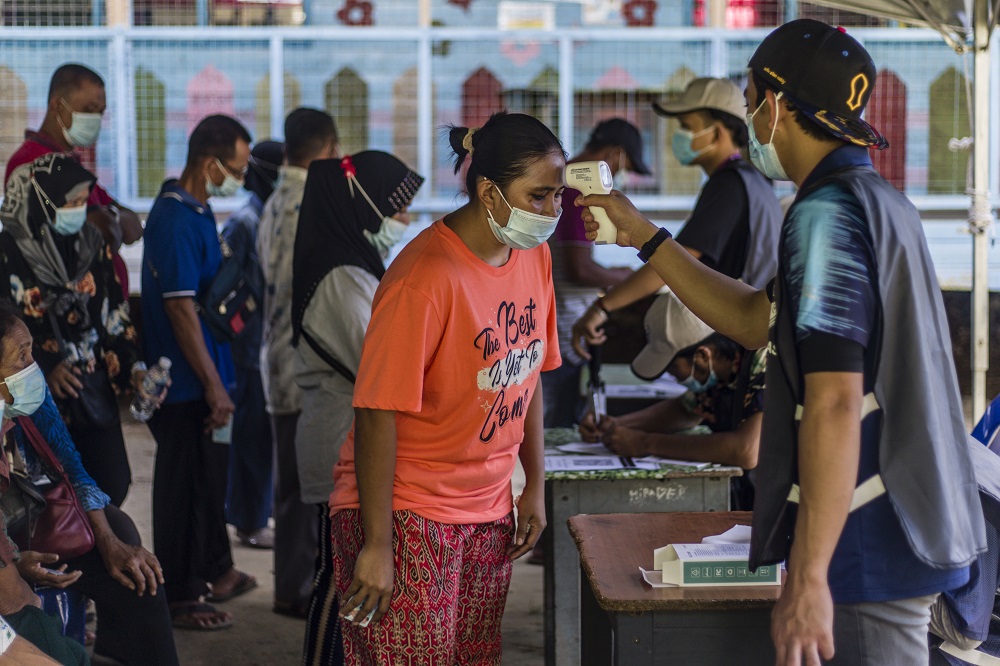 Voters get their temperatures checked before heading to the polling booths to cast their votes at SK Pulau Gaya September 26, 2020.
