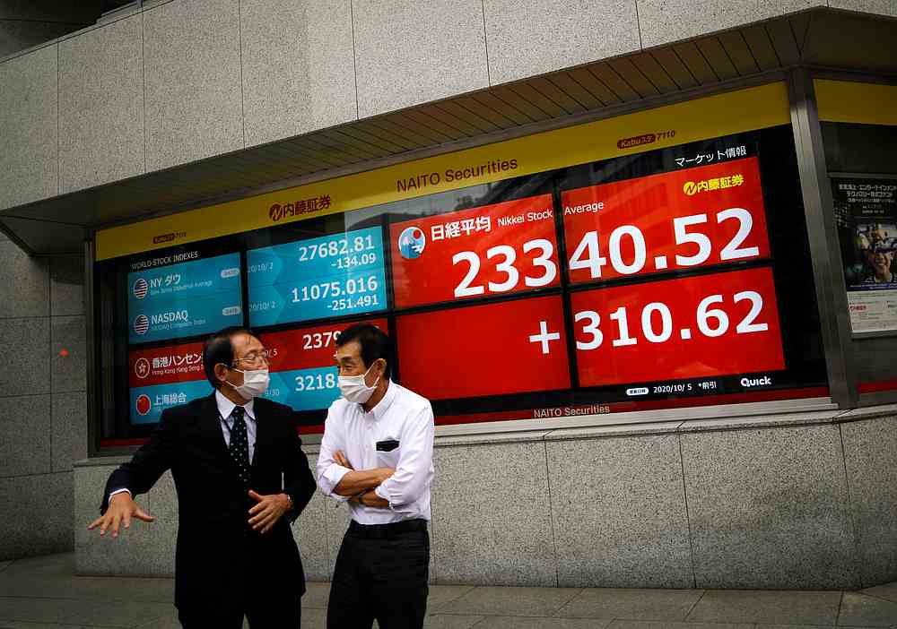 Men wearing protective face masks chat in front of a screen displaying Nikkei share average and world stock indexes outside a brokerage, amid the Covid-19 outbreak in Tokyo Octboer 5, 2020. — Reuters pic