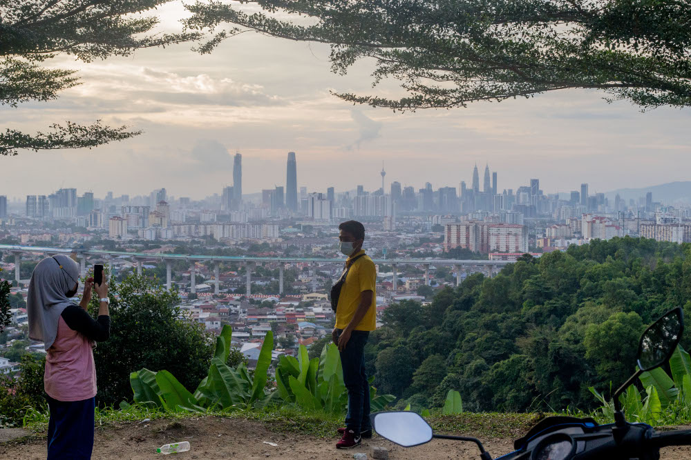People wearing face masks pose for a picture on the roadside atop a hill with a view of the Kuala Lumpur skyline in Ampang January 31, 2020. u00e2u20acu201d Picture by Firdaus Latif