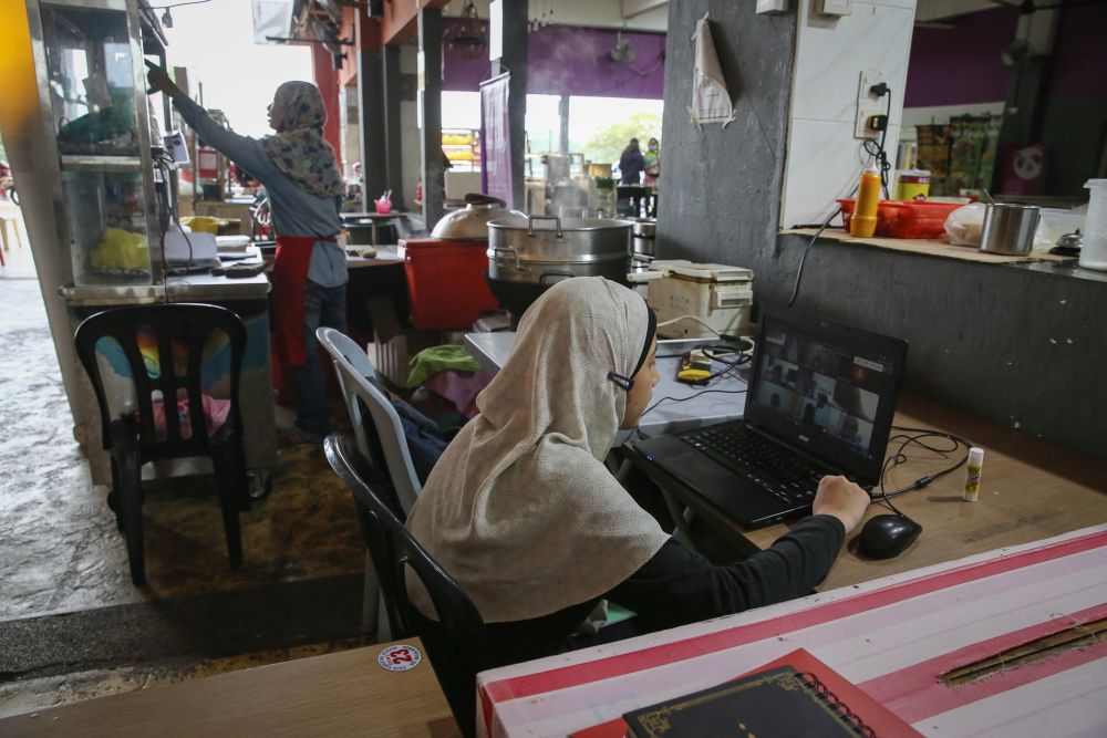 Alya Khadeeja Mohd Zaidi, a Form One school student, takes part in an online class near her mother’s food stall in Shah Alam amid movement control order January 20, 2021. — Picture by Yusof Mat Isa