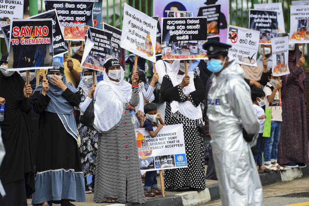 In this file photo taken December 31, 2020 a policeman stands guard as protesters hold placards during a demonstration against the government policy of forced cremations of Muslims who died of Covid-19, outside a cemetery in Colombo. u00e2u20acu201d AFP pic 