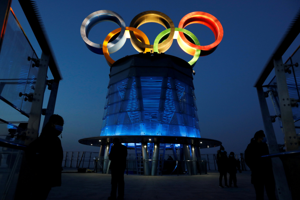 People wearing face masks are seen near the lit-up Olympic rings at top of the Olympic Tower, a year ahead of the opening of the 2022 Winter Olympic Games, in Beijing, China February 4, 2021. u00e2u20acu201d Reuters picnn