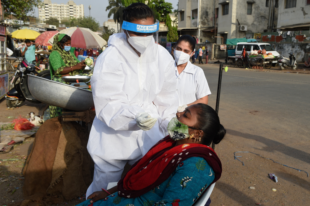 A health worker wearing protective gear collects a nasal swab sample from a woman to test for the Covid-19 coronavirus along the roadside vegetable market in Ahmedabad March 21, 2021. u00e2u20acu201d AFP picnn