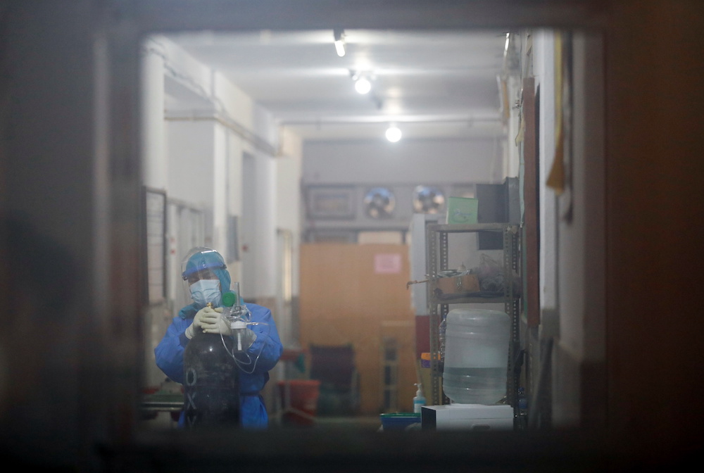 A health worker is seen through the window as he drags an oxygen cylinder towards the Covid ward as the major second wave of Covid-19 surges in Kathmandu April 26, 2021. — Reuters pic