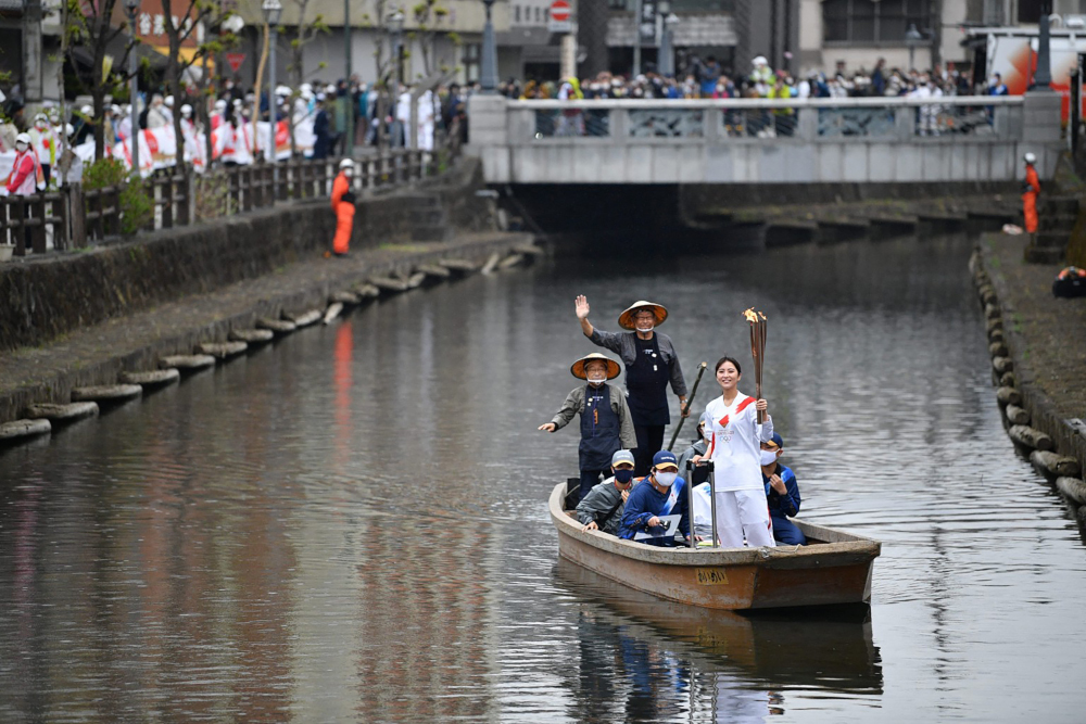 This handout photograph taken and released March 28, 2021 by Tokyo 2020 shows a Japanese torchbearer carrying the Olympic torch on a boat during the torch relay in the eastern city of Tochigi. u00e2u20acu201d Tokyo 2020 handout pic via AFP 