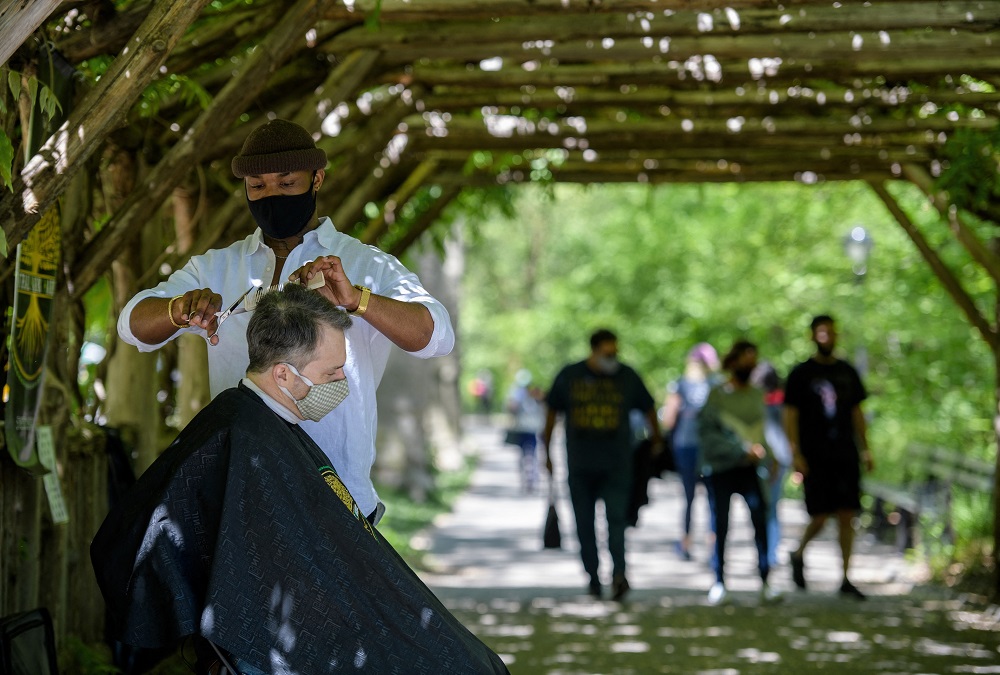 Barber Herman James cuts a client's hair under a pergola in Central Park. u00e2u20acu2022 AFP pic via ETX Studio