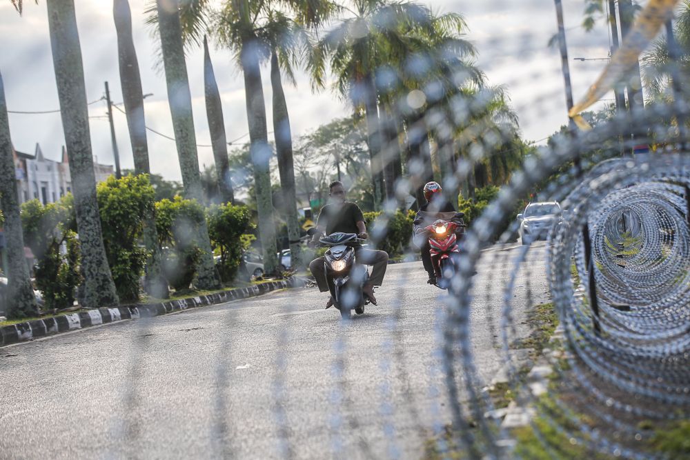 Motorists ride past barbed wire fencing amid the enhanced movement control order in Taman Meru 2b in Ipoh August 11, 2021. u00e2u20acu2022 Picture by Farhan Najib