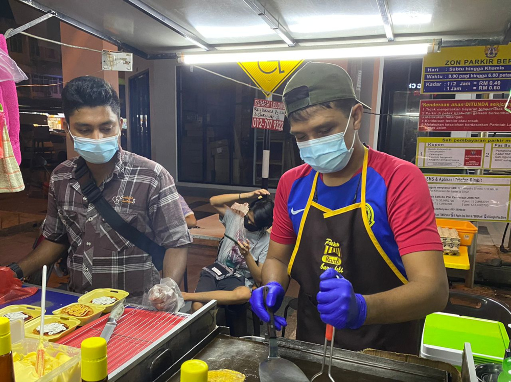 Burger stall proprietor Ahmad Lokman, 35, (right) said he will drive back with his wife to his hometown in Batu Pahat on Thursday evening. — Picture by Ben Tan