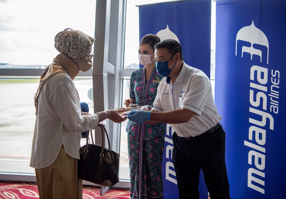 Malaysia Airlines group chief operations officer Ahmad Luqman distributes cookies to departing passengers on the first VTL flight MH603 from KLIA to Singapore, November 29, 2021. — Picture courtesy of Malaysia Airlines